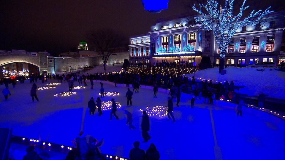 Des patineurs patinent le soir. Autour d'eux, des lumières de Noël. 