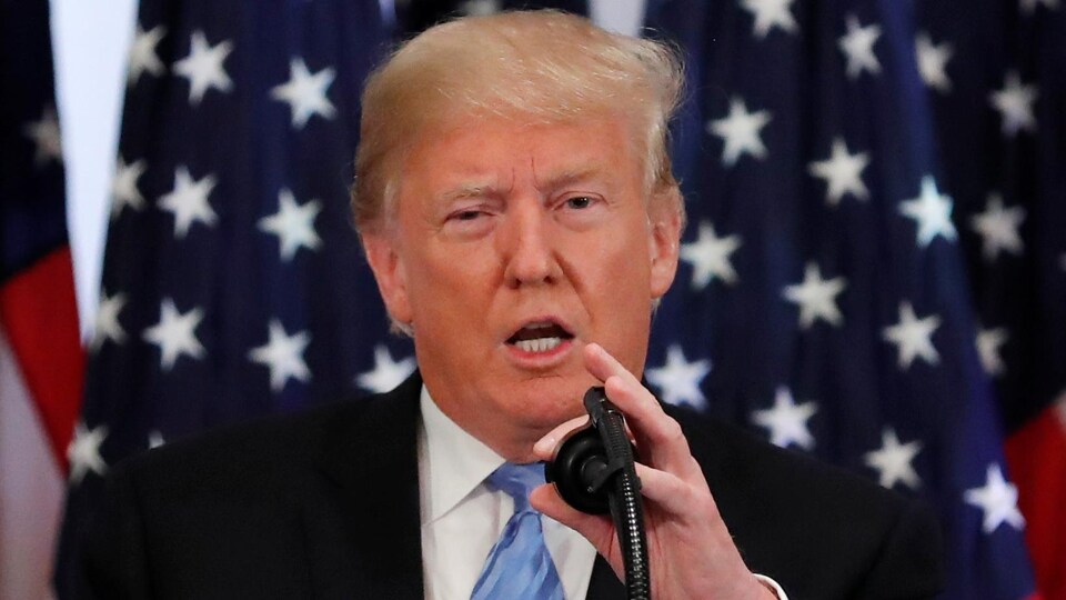 Devant plusieurs drapeaux des États-Unis, un homme en veston cravate répond aux questions à un micro.