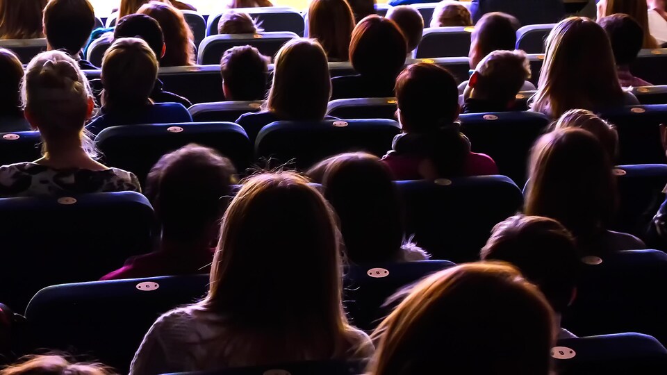 Foule dans une salle de théâtre vue de dos.