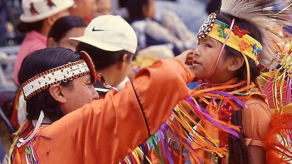 Plan moyen de Johnny Black qui ajuste le costume de son fils avant sa participation à un concours de danse autochtone dans le cadre d'un pow-wow.