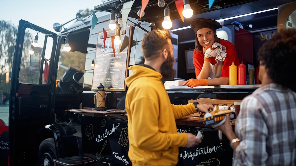 Trois personnes discutent et mangent à l'extérieur devant un comptoir de camion de restauration rapide.