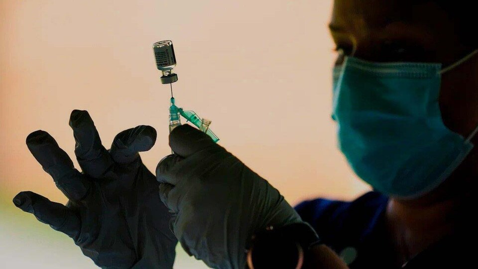 Une femme tient un vaccin entre ses mains avec des gants et porte un masque.