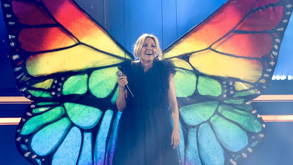 L'animatrice porte de grandes ailes de papillon multicolores sur scène. 