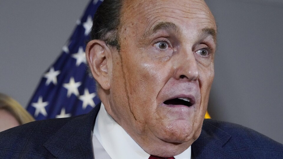 Rudy Giuliani, la bouche entrouverte, regarde les journalistes pendant que des coulisses de peinture coulent sur ses joues.