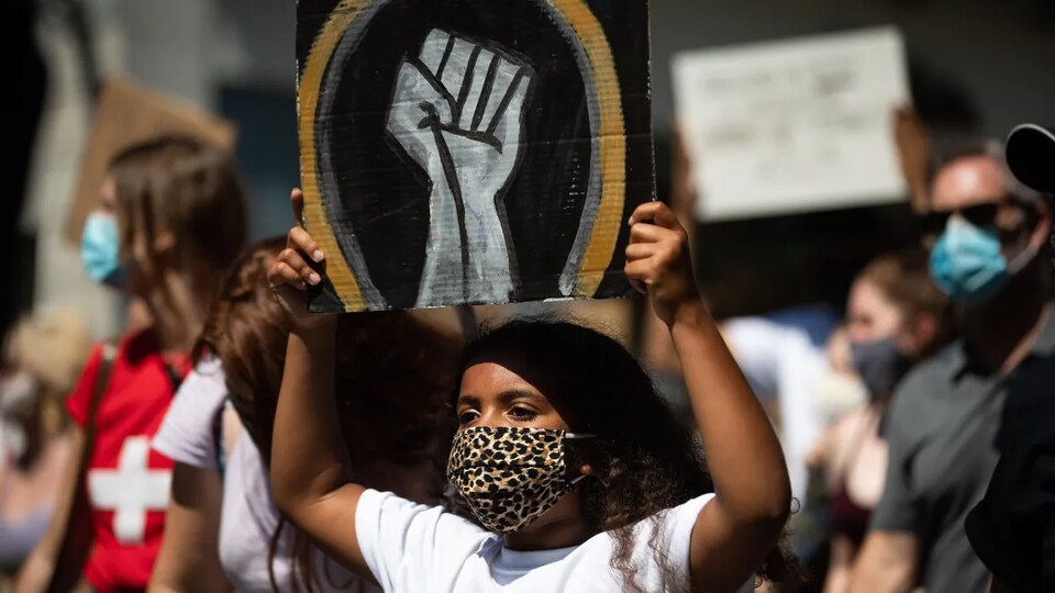 Une femme noire porte une pancarte sur laquelle figure le dessin d'un poing levé, le logo du mouvement Black Lives Matter.
