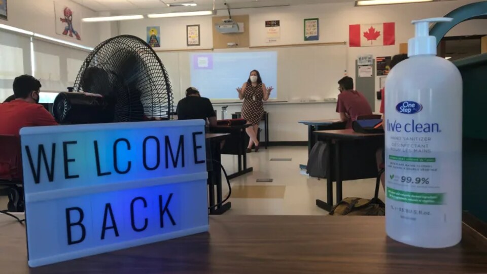 Une salle de classe avec au premier plan un gel désinfectant et une affiche sur laquelle il est écrit "Welcome back".