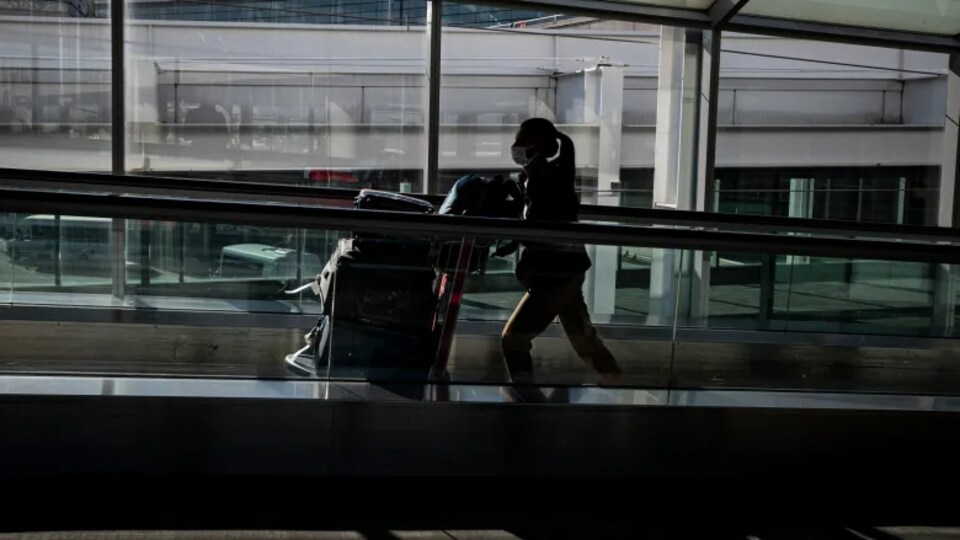 Une voyageuse pousse ses bagages sur un tapis roulant dans un aéroport.