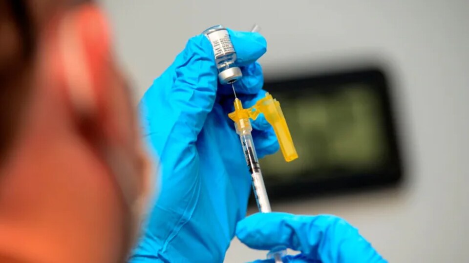 Quelqu'un portant des gants médico-chirurgicaux rempli une seringue de vaccin pfizer bivalent à partir d'une dose embouteillée.