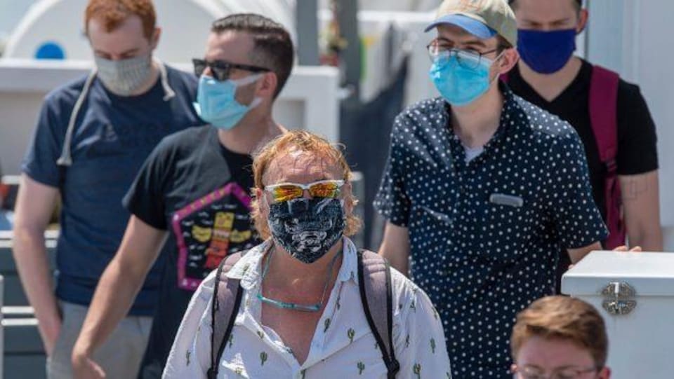 Des gens portant le masque marchent sur un trottoir en été.