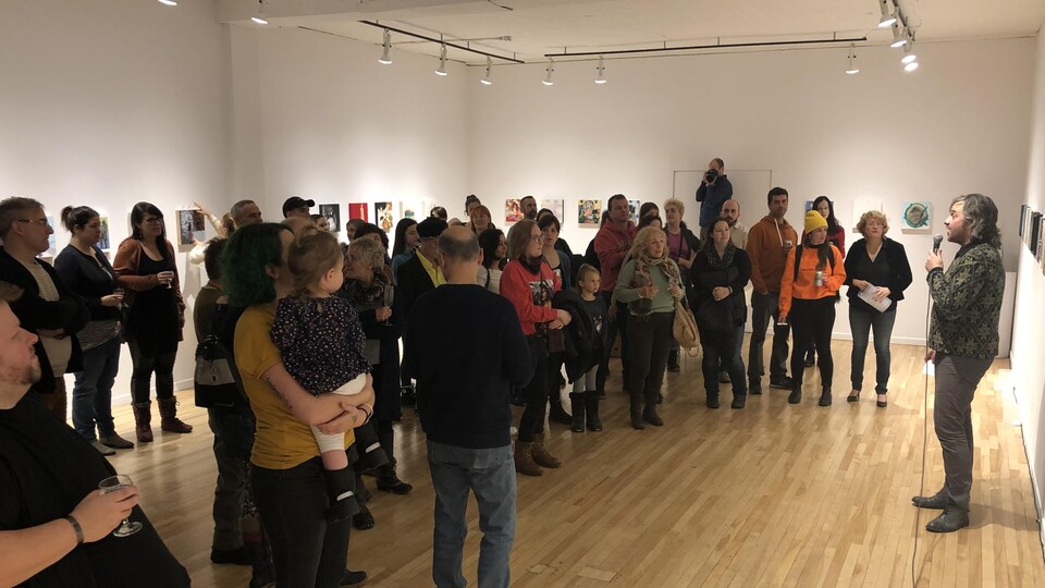 Des gens dans une salle d'exposition écoutent quelqu'un parler au micro devant eux.