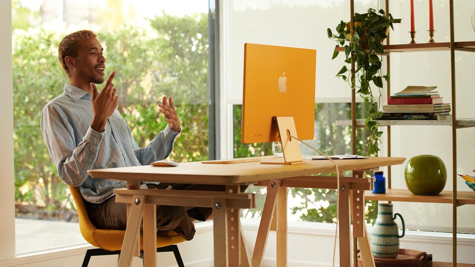 Un homme parle devant son écran d'ordinateur, posé sur un bureau.