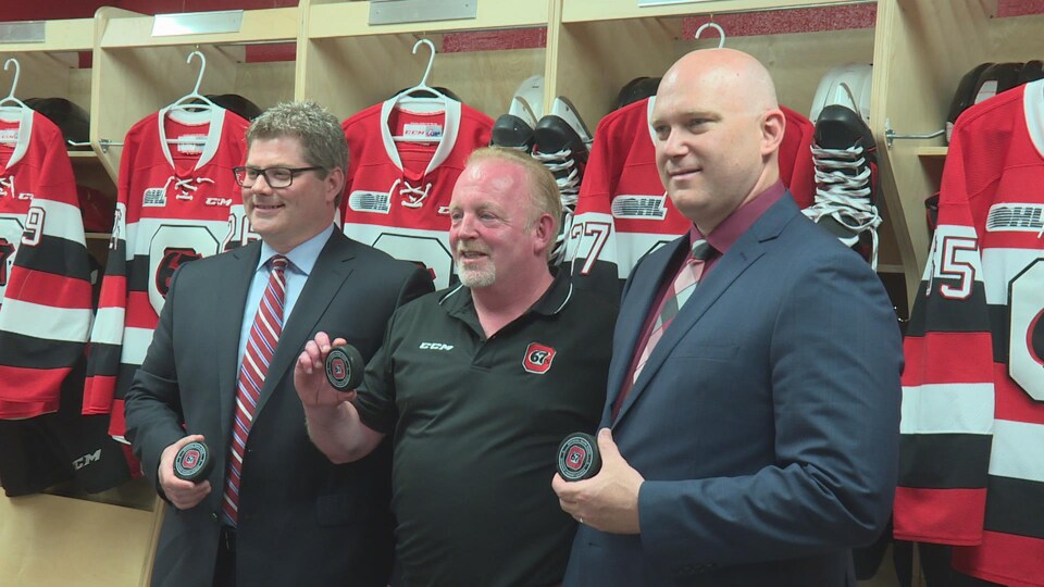 James Boyd, Jeff Hunt et André Tourigny posent avec une rondelle de hockey dans les mains.