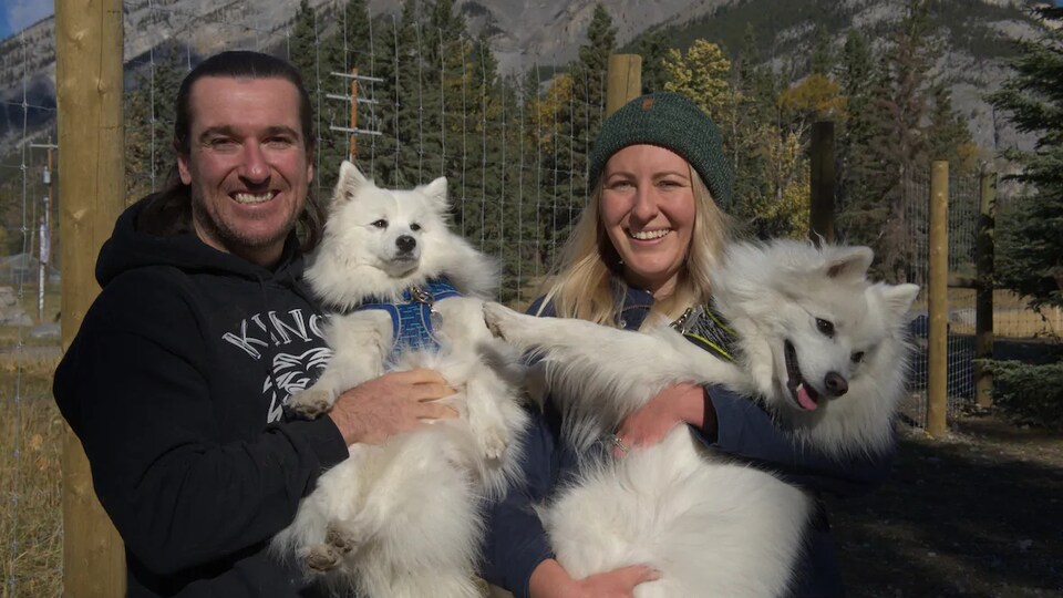 Un homme et une femme portent chacun un chien devant une clôture.