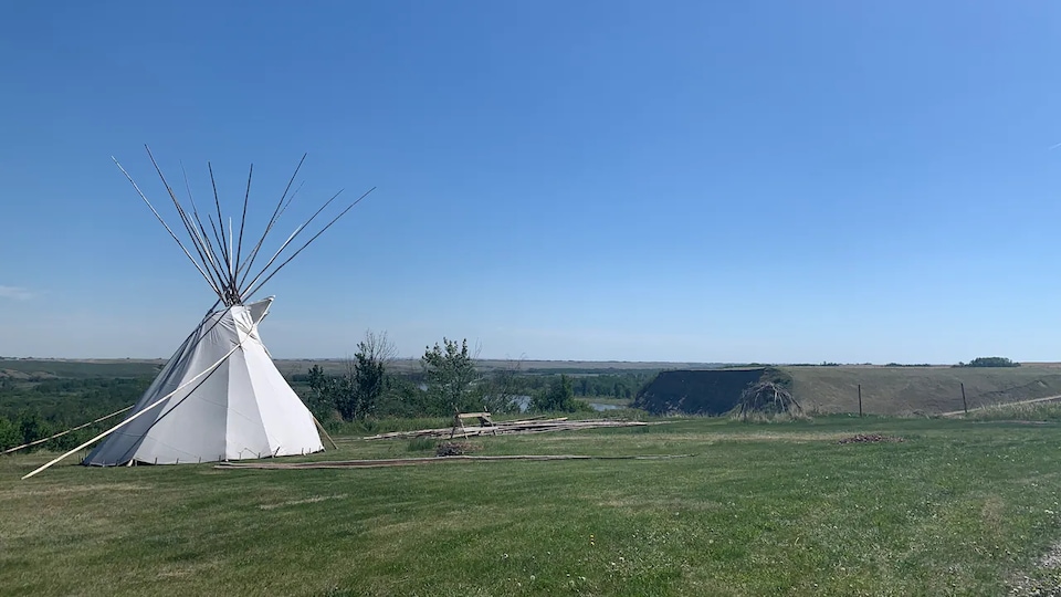 Un tipi sur une plaine, près d'une rivière, sous un ciel dégagé.