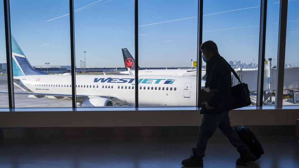 Un passager passe devant une fenêtre derrière laquelle se trouvent un avion de WestJet et un appareil d'Air Canada à l'Aéroport international de Calgary (YYC), en Alberta, le mercredi 31 août 2022.