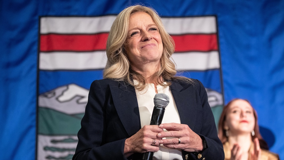 La cheffe du Nouveau Parti démocratique de l'Alberta, Rachel Notley sourit devant le drapeau albertain.