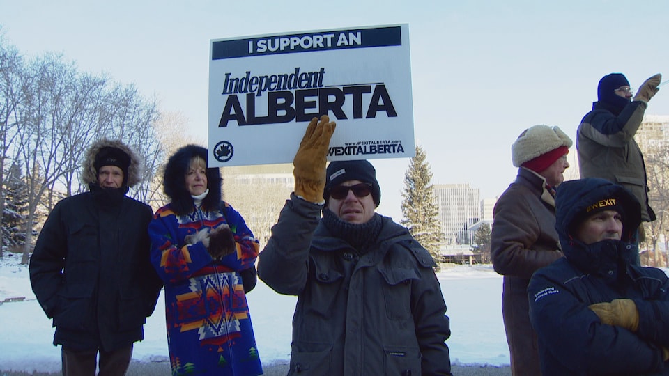 Quelques-uns des manifestants se tiennent debout, dehors, en hiver. L'un d'eux tient une affiche sur laquelle il est écrit, en anglais, «je soutiens l'indépendance de l'Alberta».