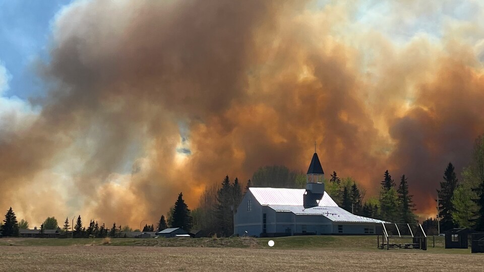 Un panache de fumée causé par un feu de forêt s'élève au-dessus d'une église dans le sud d'Entwistle, en Alberta, le vendredi 5 mai 2023.
