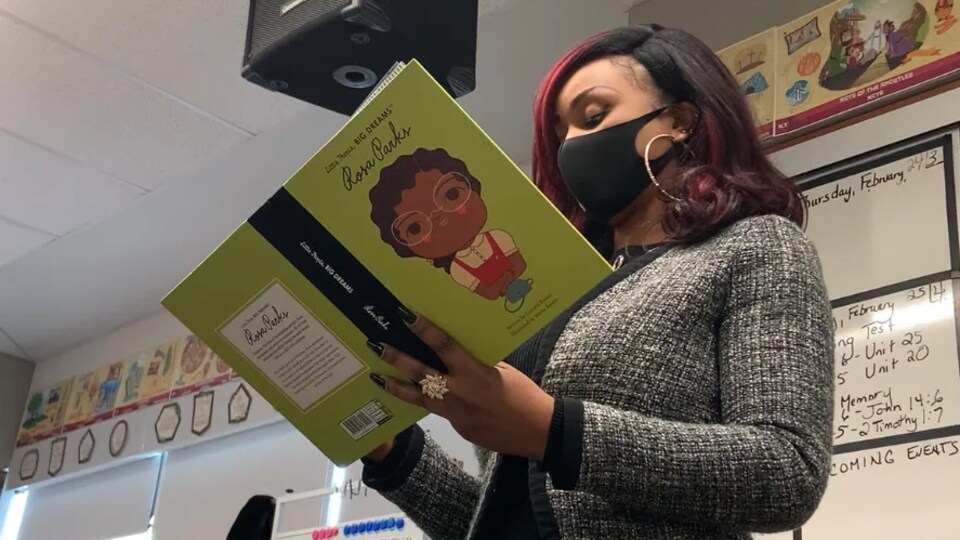 Jibs Abitoye, debout, lit un livre pour enfants dans une salle de classe.