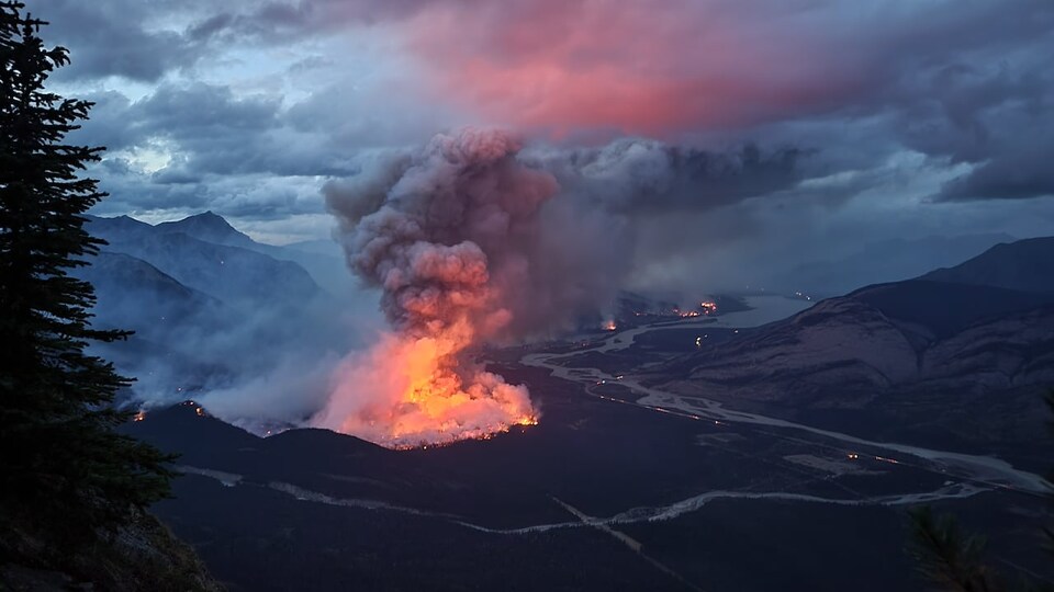 Un panache de fumée rougi par les flammes s'élève d'un feu de forêt près d'une rivière, entre des montagnes, dans le parc national Jasper, au début de septembre 2022.
