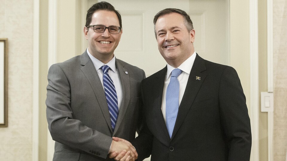 Le premier ministre albertain, Jason Kenney (à droite), serre la main du nouveau ministre de l'Éducation supérieure, Demetrios Nicolaides (à gauche), après la prestation de serment à Edmonton, le mardi 30 avril 2019. Les deux hommes en complet regardent la caméra en se serrant la main droite.