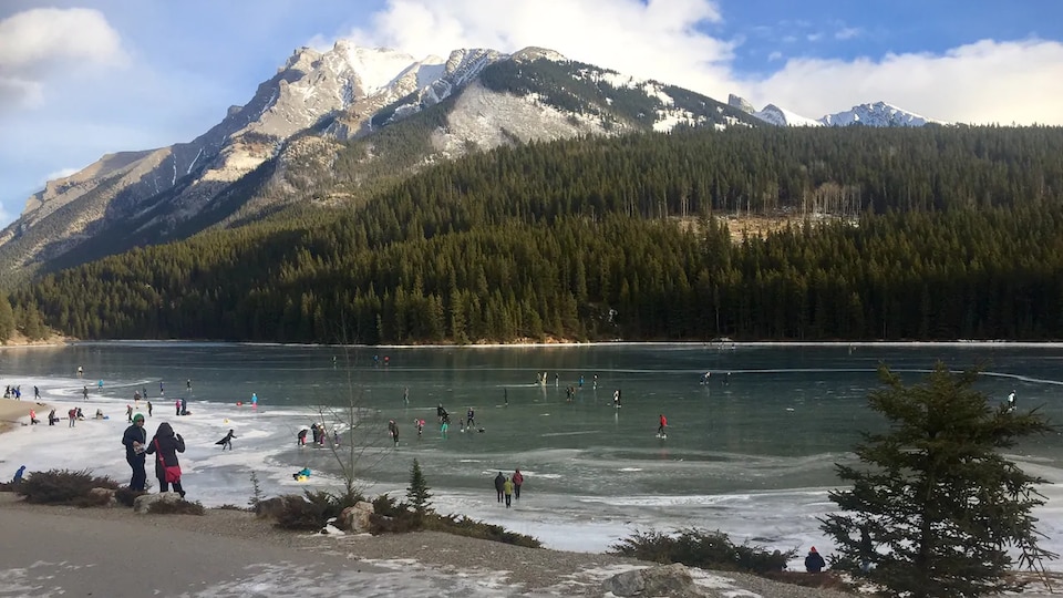 Des gens patinent sur un lac gelé, au pied d'une montagne.