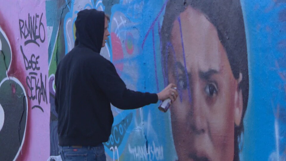 Un jeune homme peint des lettres sur une murale avec de la peinture en aérosol.
