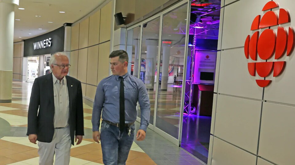 Deux hommes déambulent sur le plancher carrelé d'un centre commercial.