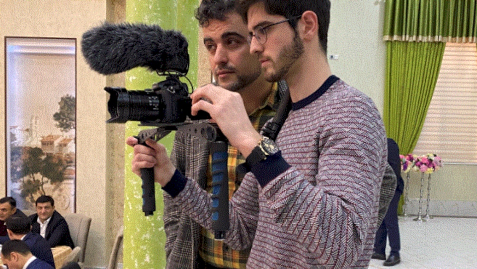 Abbasli Ehrun in a room holds the camera next to another person.