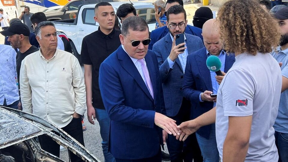 Abdelhamid Dbeibah shook hands with a man near the burned car. 