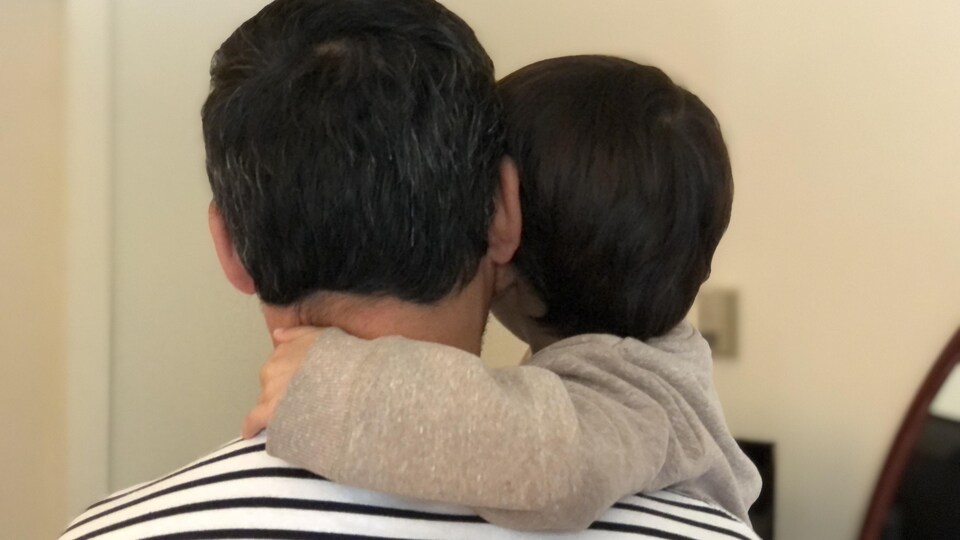 Un homme vu de dos tient son enfant dans ses bras.