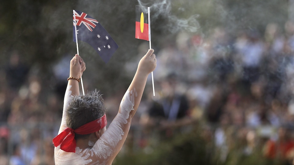 Un jeune Aborigène tient les drapeaux de l'Australie et des Aborigènes lors de célébrations en janvier 2020.