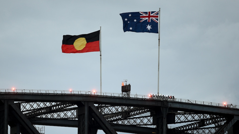 Deux drapeaux flottent au-dessus d'un pont par une journée ennuagée.
