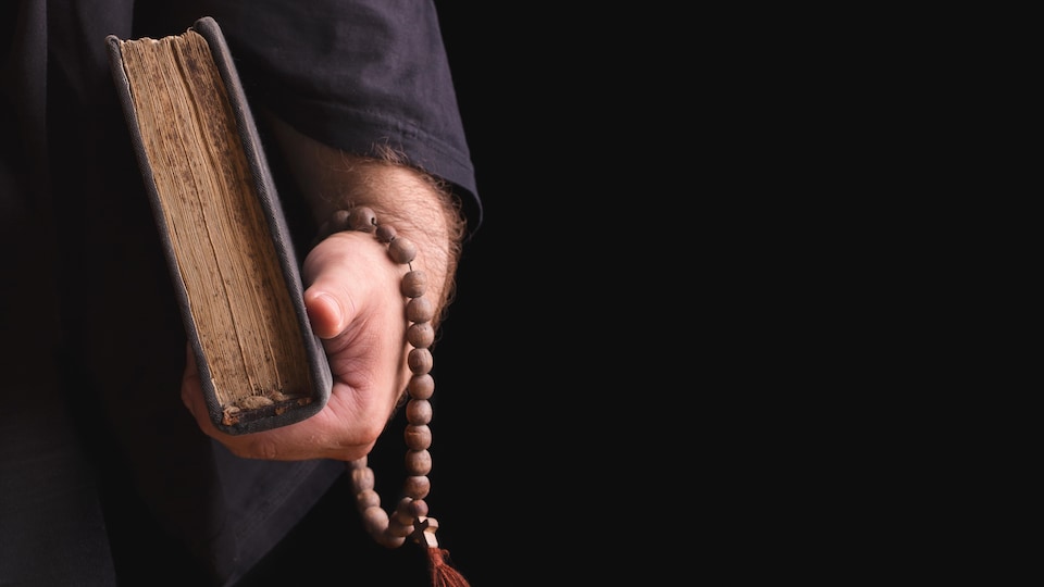 Un homme tenant un rosaire et un livre dans la main.