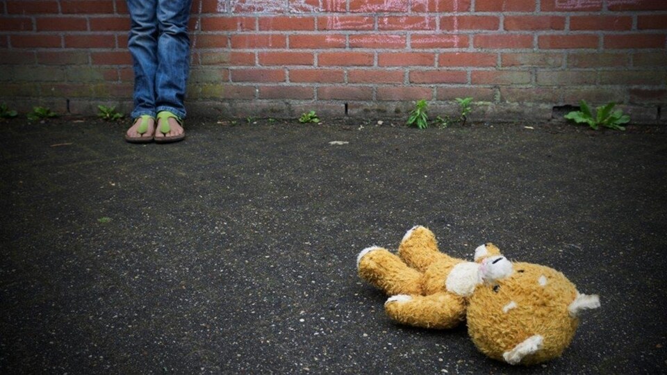 Un toutou repose au sol devant un enfant que l'on voit partiellement.