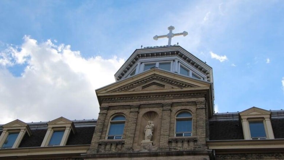 Le sommet d'un édifice avec une statue de la Vierge à l'engfant et une croix surplombant le toit.