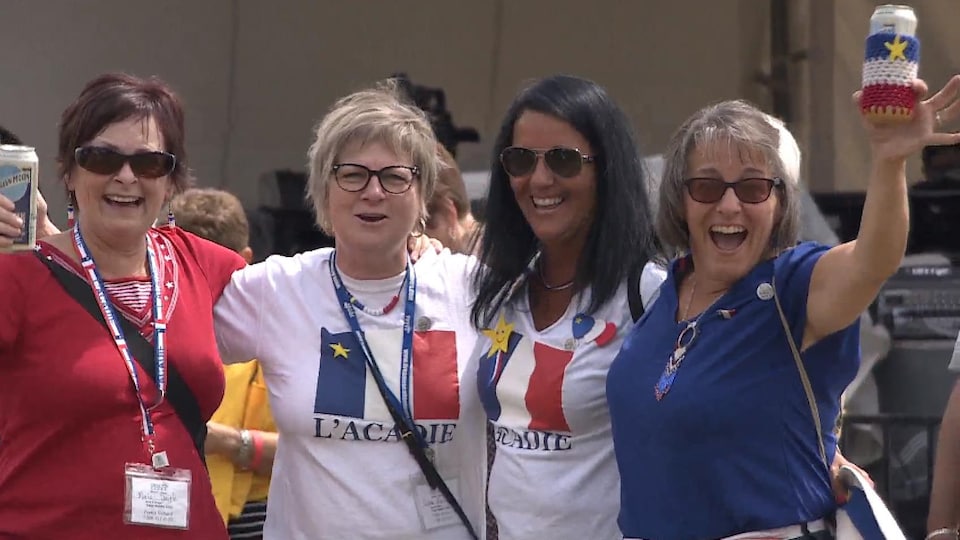 Quatre femmes sourient à la caméra et portent des vêtements aux couleurs du drapeau acadien.