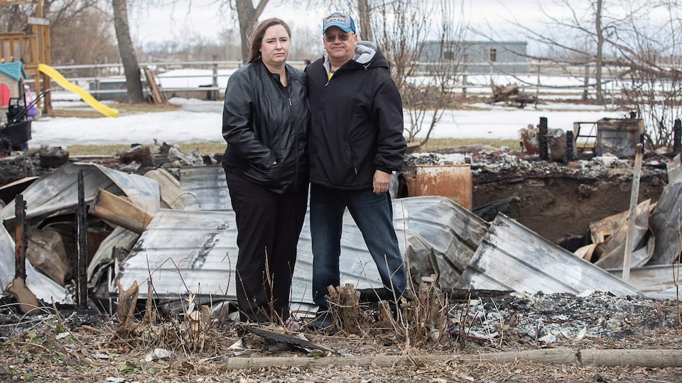 Un homme et une femme debout devant une maison incendiée.