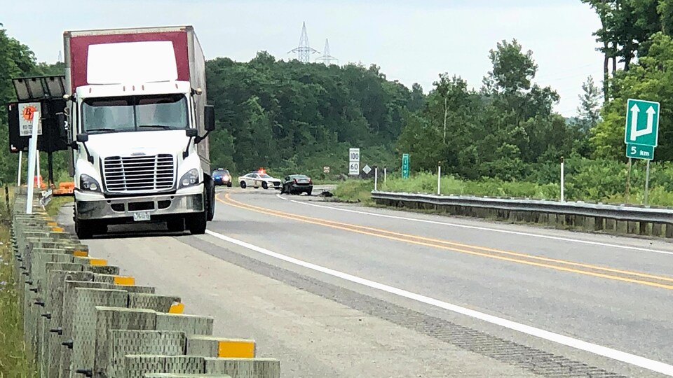 Derrière le camion, deux véhicules de police sont stationnés à côté de l'automobile accidentée.