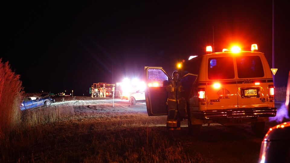 Une automobile bleue est dans le terre-plein. Plusieurs véhicules d'urgence sont stationnés à proximité.