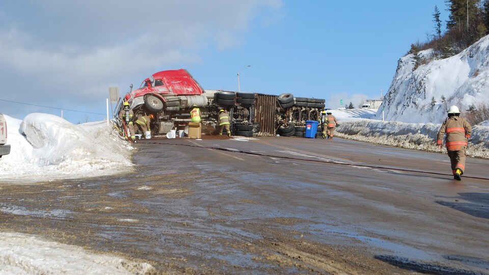 Un camion rouge renversé au milieu de la route 138.