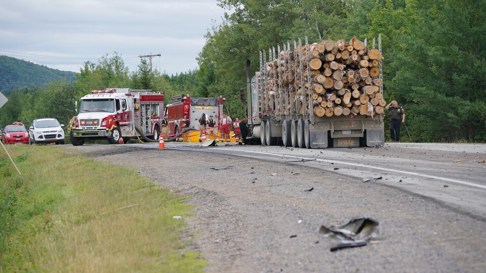 Des camions de pompiers et un camion de bois sur la route avec des débris.