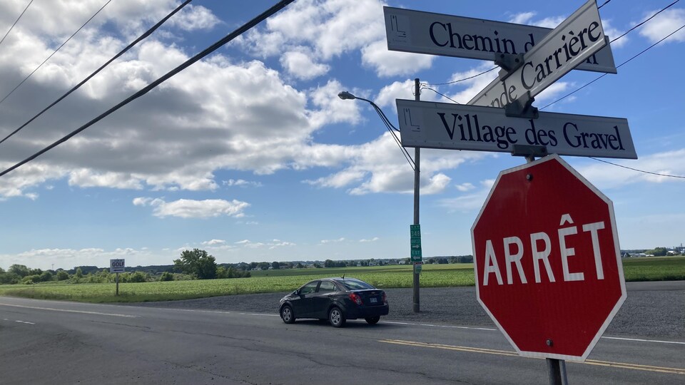 Un panneau d'arrêt avec une voiture en arrière plan.
