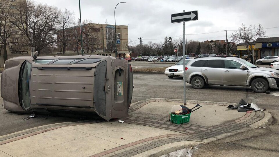 Un véhicule renversé sur le côté au coin d'une rue, devant la voiture qui l'a emboutie et une autopatrouille.