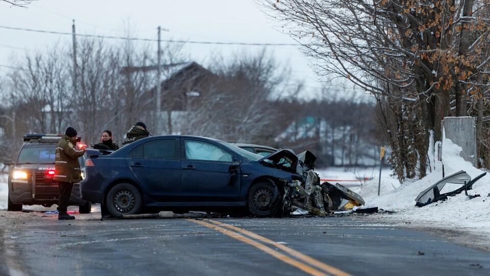 Des policiers attroupés autour d'un véhicule lourdement endommagé par un accident, l'hiver.