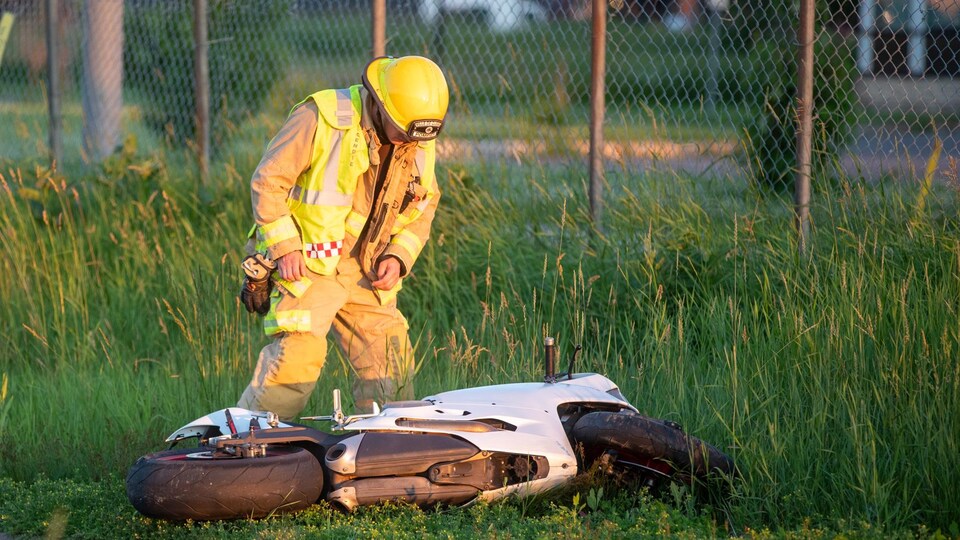 Un premier répondant observe la motocyclette accidentée sur le bord de la route.