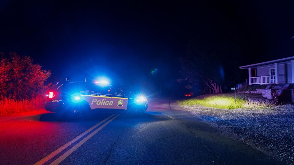 Une voiture de police est arrêtée sur une route en pleine nuit. 