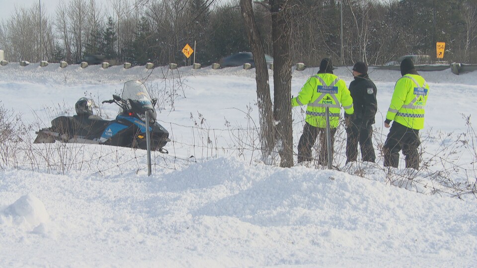 Des agents provinciaux et un policier sur un terrain enneigé près d'une motoneige