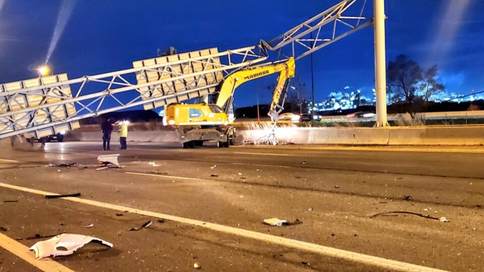Des débris sur la chaussée avec en arrière-plan le panneau de signalisation écroulé et la pelle mécanique.