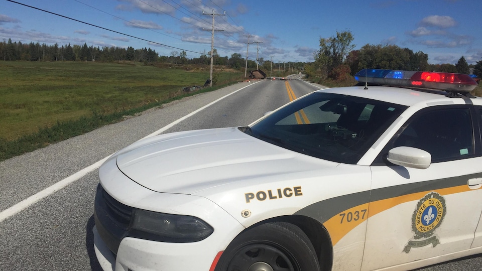 Une voiture de police barre la route d'un accident en arrière-plan.